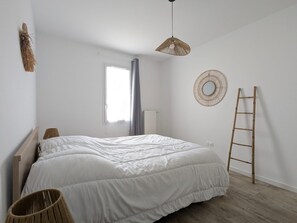 Een slaapkamer met een bed, een raam, een hanglamp, een spiegel aan de muur en een houten ladder.