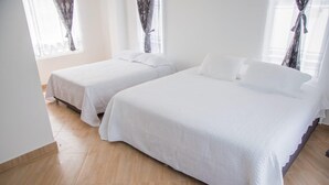 Ein Hotelzimmer mit zwei Betten, Holzboden und Vorhängen an den Fenstern.