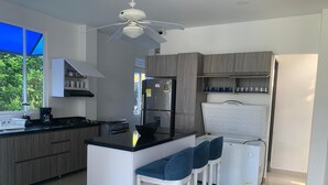 Eine moderne Küche mit einer zentralen Kochinsel, Barhocker, Deckenventilator und Kühlschrank.