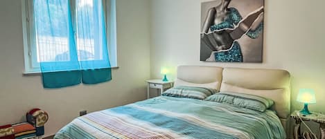 Quarto com cama, duas mesas de cabeceira com luminárias, janela com cortinas e uma obra de arte pendurada na parede.