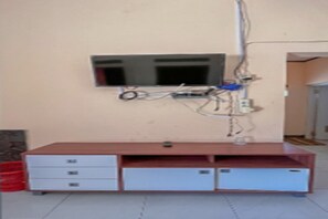 A room with a TV mounted on the wall, a wooden cabinet with drawers, and visible electrical wiring. - Cozzy Villa Family B (Pangalengan)
