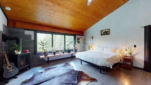 A bedroom with a bed, a guitar, a fireplace, and a large window. - Okanagan - Alpine Chalet (Christina Lake)