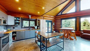 L’intérieur d’une cabane en rondins comprend une cuisine, un coin repas et de grandes fenêtres.