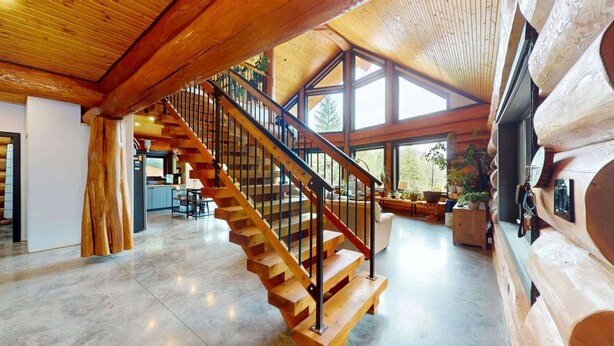 Un intérieur spacieux avec un escalier en bois, de grandes fenêtres et un coin salon confortable.