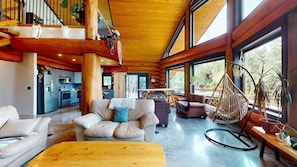 A spacious interior with a wooden ceiling, large windows, a kitchen, and a seating area with a hanging chair. - Okanagan - Alpine Chalet (Christina Lake)