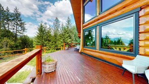 Une terrasse en bois avec une chaise en bois, un bac à fleurs en bois et une vue sur une forêt et des montagnes.