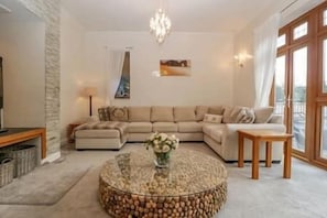 A living room with a sectional sofa, a round coffee table, and a chandelier. - Luxury6BedHouse-HotTub-GamesRoom (Poole)