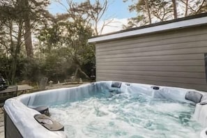 A hot tub with a wooden deck and a covered area, surrounded by trees. - Luxury6BedHouse-HotTub-GamesRoom (Poole)