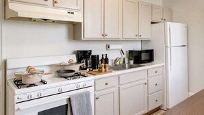 Una cocina con armarios blancos, estufa, microondas y refrigerador.