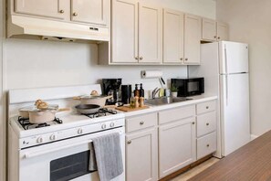 Una cocina con armarios blancos, estufa, microondas y refrigerador.
