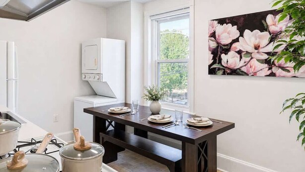 Una cocina moderna con una mesa de comedor preparada para cuatro personas, horno empotrado y ventana con vistas a árboles.
