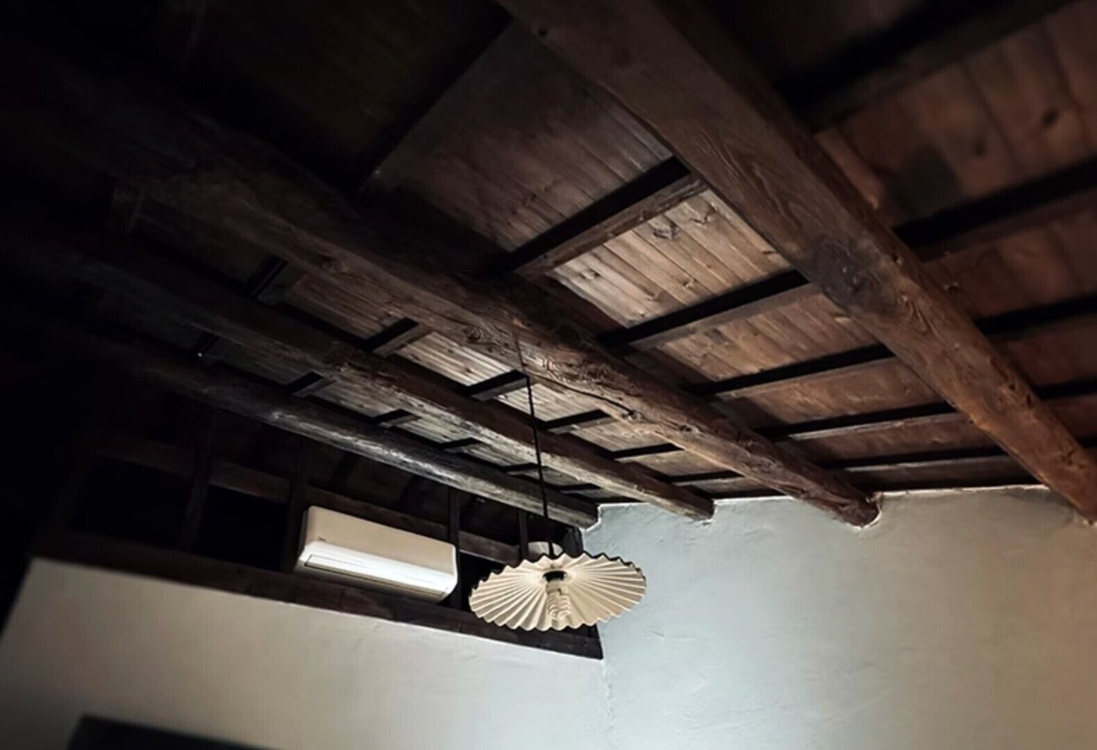 A rustic ceiling with exposed wooden beams and a single hanging light fixture.