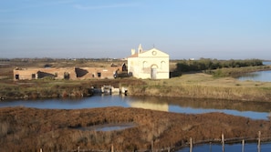 A building with a bell tower, surrounded by a water body and vegetation.