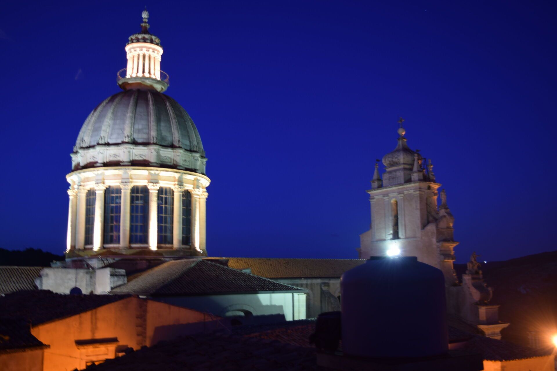 Un edificio grande con cúpula y una estructura más pequeña contigua, ambos iluminados contra un cielo oscuro.