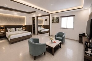 A modern hotel room with a large bed, two armchairs, a coffee table, a TV, and a large window.