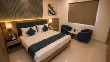 A hotel room with a large bed, bedside tables, a desk, two chairs, a painting on the wall, and a window with a blind.