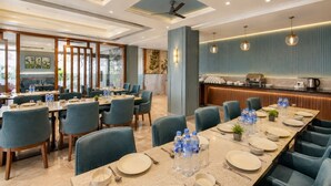 A hotel dining area with multiple tables, chairs, and a kitchen in the background. - Hotel Salt and Rove Near Delhi Airport (New Delhi)