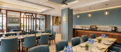Une salle à manger d’hôtel avec plusieurs tables, des chaises et une cuisine en arrière-plan.