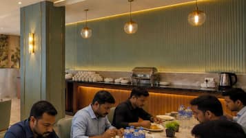 A group of people dining in a modern restaurant with a high ceiling, pendant lighting, and a buffet setup in the background.