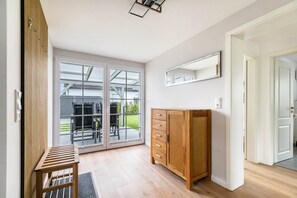 Ein Zimmer mit Holzschrank, einer Bank, einer Schiebetür zu einem Außenbereich und einem wandmontierten Spiegel.