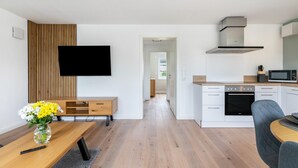 Una cucina moderna con mobili bianchi, un forno a microonde e un piano cottura. C'è una zona pranzo con un tavolo e sedie. Un televisore a schermo piatto è montato a parete.