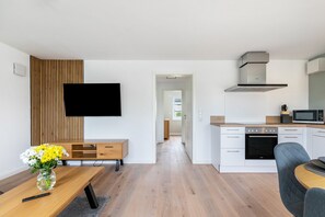 Eine moderne Küche mit weißen Schränken, einer Mikrowelle und einem Herd. Es gibt einen Essbereich mit Tisch und Stühlen. Ein Flachbildfernseher ist an der Wand montiert.