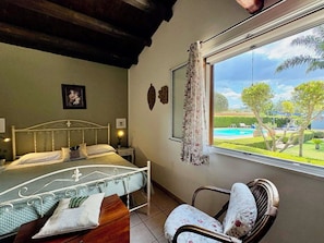 Ein Schlafzimmer mit Bett, einem Sessel, einem Fenster mit Blick auf Pool und Garten.