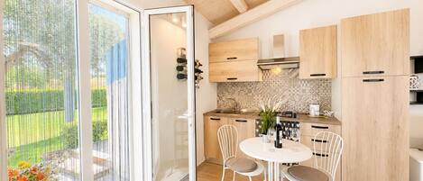 A modern kitchen with wooden cabinets, a dining area with white chairs, and a sliding glass door leading to a garden.