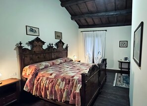 A bedroom with a wooden bed, a nightstand, a bedside table, a lamp, a window with curtains, and a framed picture on the wall. - 'Falco' Room with Wi-Fi and Air Conditioning (Taglio di Po)