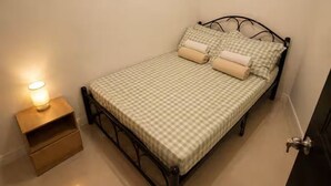 Un lit simple avec une couvre-lit à carreaux, deux oreillers, une table de chevet avec une lampe et une porte sur la droite.