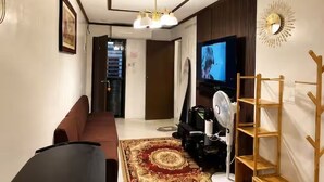 Un salon avec un canapé, un téléviseur, un ventilateur et une étagère en bois.