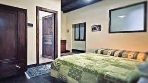 Una camera da letto con un letto, una porta in legno, una cassettiera, uno specchio e un quadro appeso al muro.