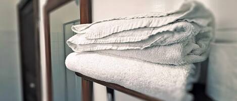 A stack of white towels on a wooden shelf in a bathroom with a mirror.