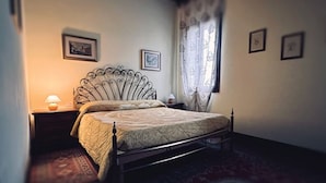 A bedroom with a metal-framed bed, a bedside table with a lamp, and a window with curtains. - 'Picchio' Room with Wi-Fi and Air Conditioning (Taglio di Po)