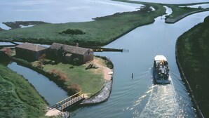 A boat on a calm river with a bridge and a building on the bank. - 'Picchio' Room with Wi-Fi and Air Conditioning (Taglio di Po)