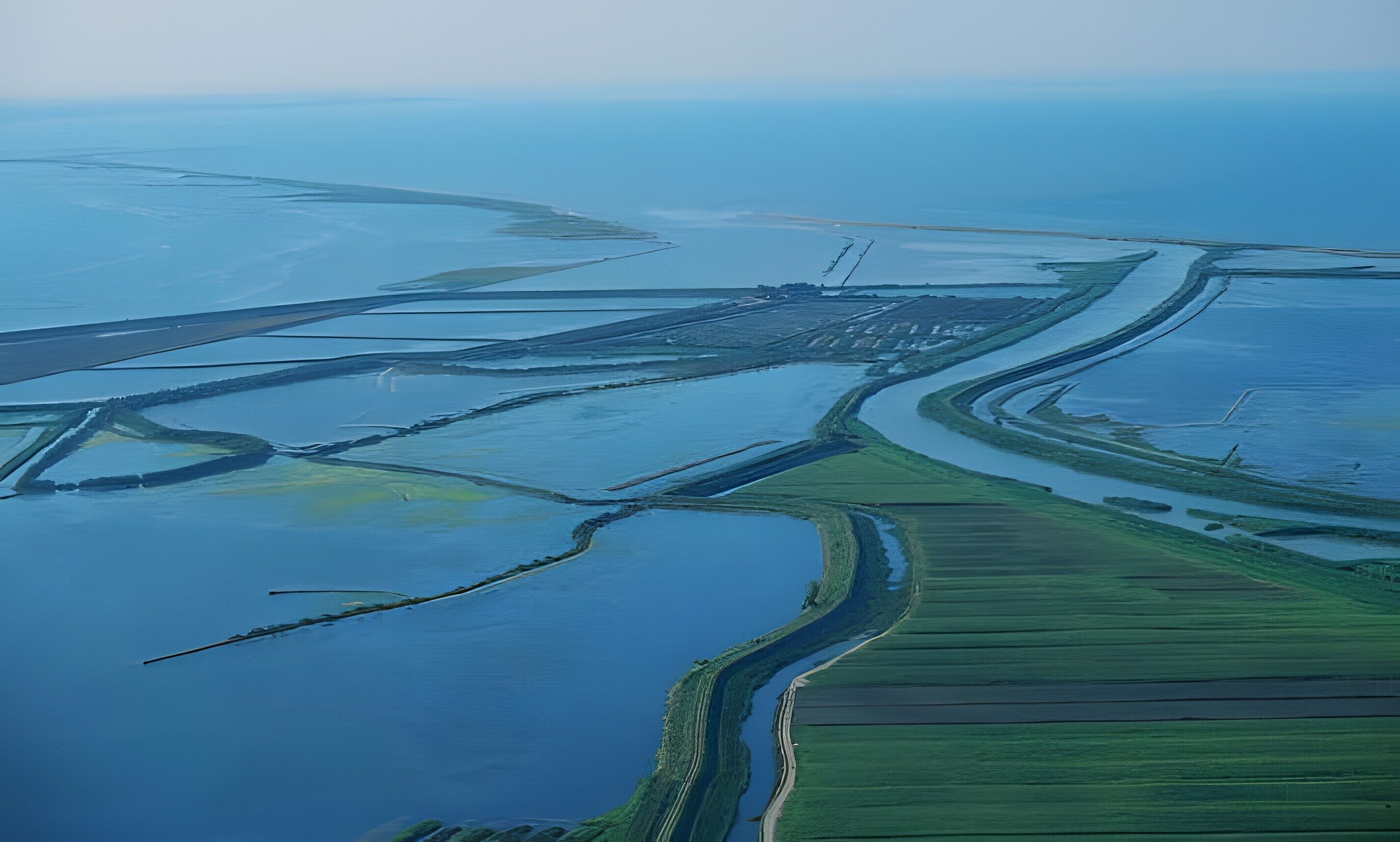 An aerial view of a coastal landscape with water channels, green fields, and a distant structure.