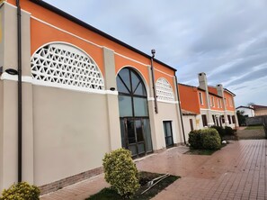 A building with a beige facade, large arched windows, and a brick pathway.