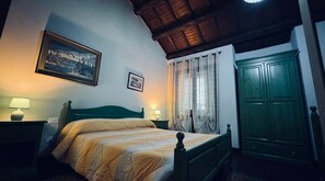 Un dormitorio con una cama, dos mesitas de noche con lámparas, un cabecero de madera, una puerta verde y dos cuadros enmarcados en la pared.