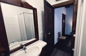 Een badkamer met een wit wastafel, een spiegel en een deur naar een gang.