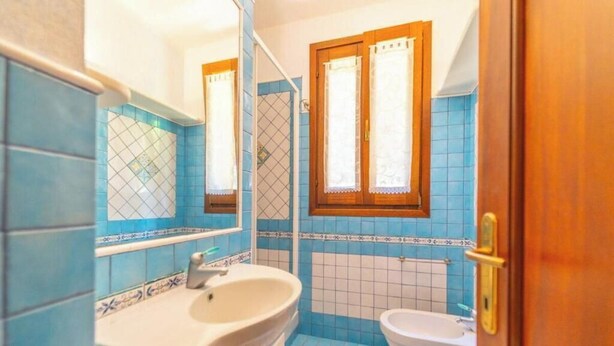 Een badkamer met blauwe tegels, een wastafel, een spiegel en een raam met gordijnen.
