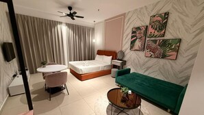 A modern bedroom with a bed, a green sofa, a round coffee table, a small table with a lamp, and a ceiling fan. - Portrait Resort Port Dickson (Port Dickson)