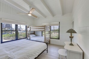 Ein Zimmer mit Etagenbetten, einem Deckenventilator, einem Tisch mit Lampe und großen Fenstern.