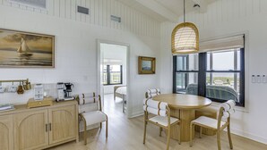 A dining area with a round wooden table, white upholstered chairs, a wicker pendant light, and a painting of a sailboat on the wall. - Casa Del Mare | Beach to Bay on Alligator Point (Alligator Point)