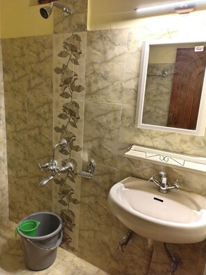 A bathroom with a sink, a shower with a handheld showerhead, and a bucket. - HS GROUP OF HOTEL (Manali)