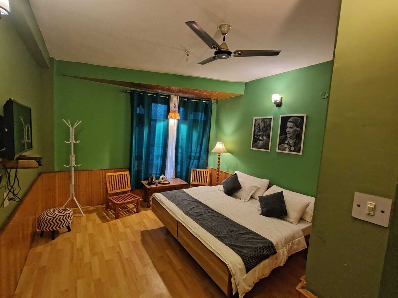 A room with a bed, a desk, a chair, a coat rack, and a ceiling fan.