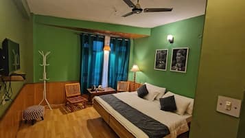 A room with a bed, a desk, a chair, a coat rack, and a ceiling fan.