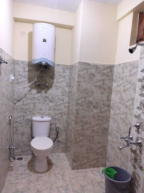 A bathroom with a toilet, a shower, and a toilet paper holder. - HS GROUP OF HOTEL (Manali)
