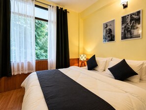 A hotel room with a bed, a window with curtains, a lamp, and two framed pictures on the wall. - HS GROUP OF HOTEL (Manali)