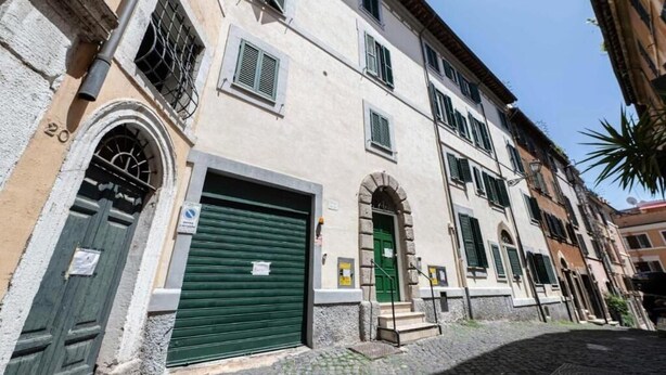 Una stretta strada acciottolata fiancheggiata da edifici storici, una porta con persiane verdi e il numero '20' ben visibile su un palazzo.