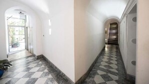 Un corridoio con pavimento a scacchi, pareti bianche e una scala che conduce a un piano superiore.